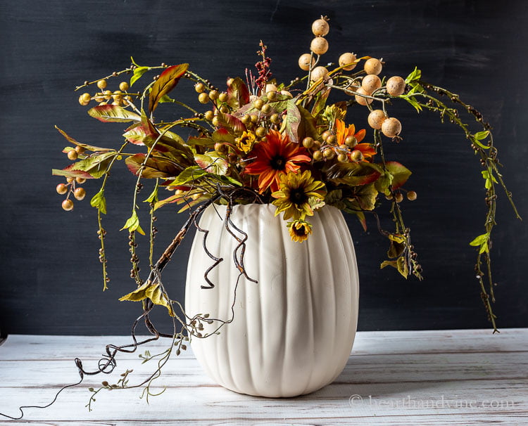 White pumpkin vase with several fall colored artificial flowers, berries and vines.