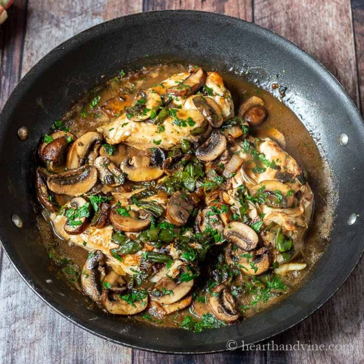 Chicken with mushrooms and shishito peppers in a skillet.