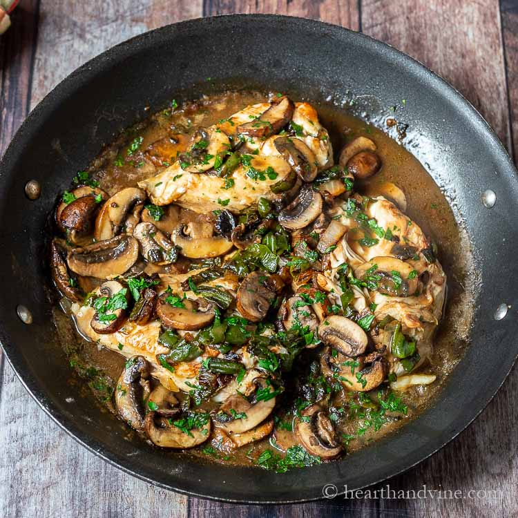 Large skillet with chicken breasts, mushrooms, shishito peppers and parsley in a gravy.