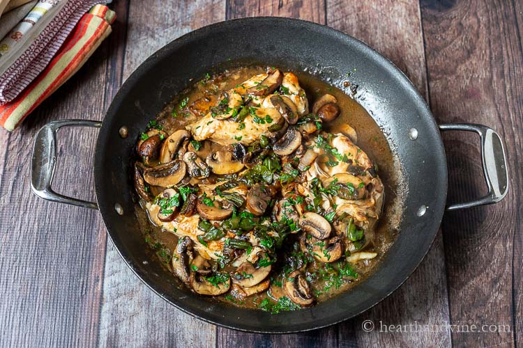 Completed recipe of skillet chicken breasts, mushrooms, shishito peppers and parsley in a large skillet.