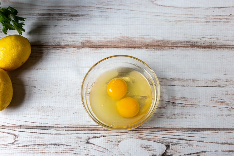 Glass bowl with two eggs inside and lemon juice.
