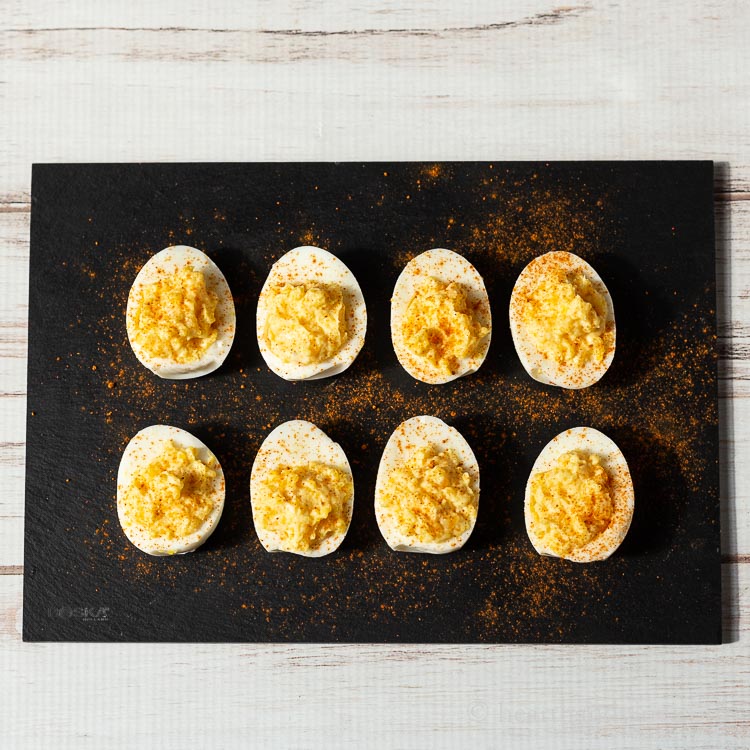 Two rows of deviled eggs on a black slate.