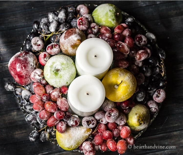 Aerial view of white candles surrounded by sugared fruit on a round glass tray.