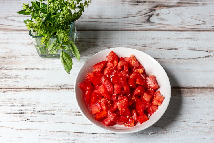 Fresh basil in a jar next to a bowl of fresh chopped tomatoes.