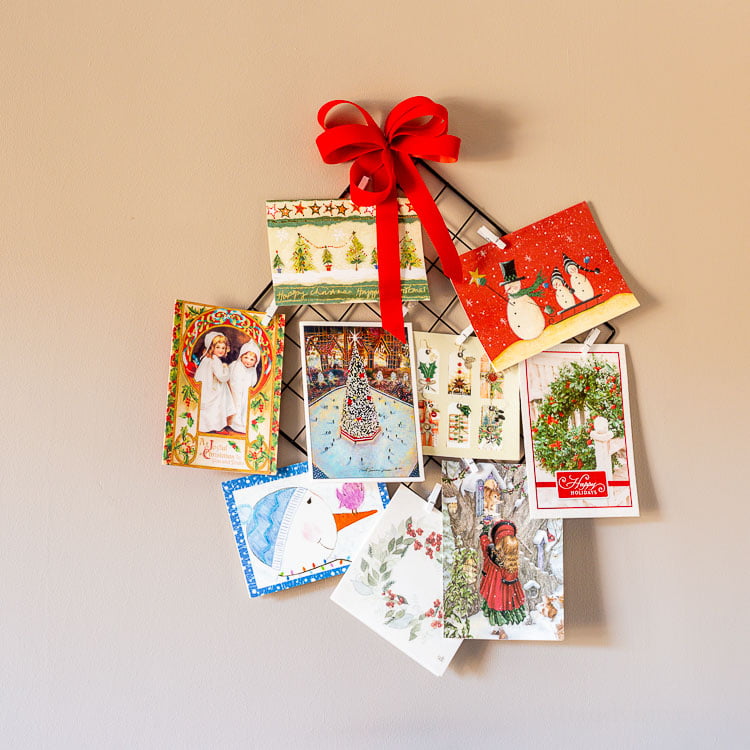 Hanging Christmas card holder with a red bow and several cards on the wall.