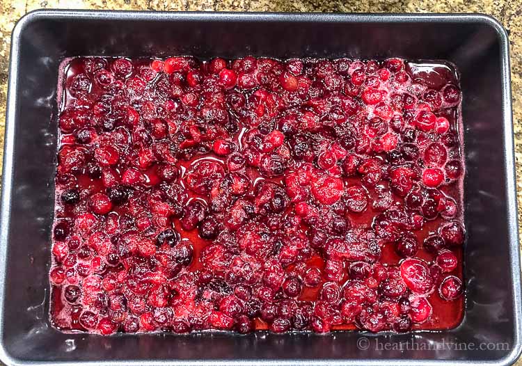 A layer of cooked fresh cranberries on the bottom of a dark 9 x 13 inch baking pan.