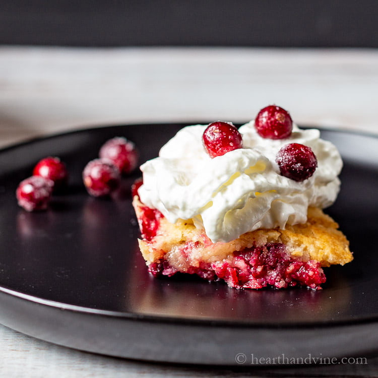 A slice of homemade cranberry dump cake topped with cream and more sugared cranberries.