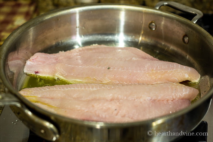 Two large red snapper fillet sautéing in a pan of olive oil.