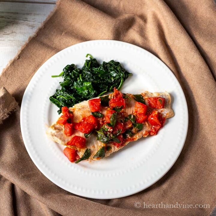Pan seared fish with tomatoes and basil on a plate with spinach.