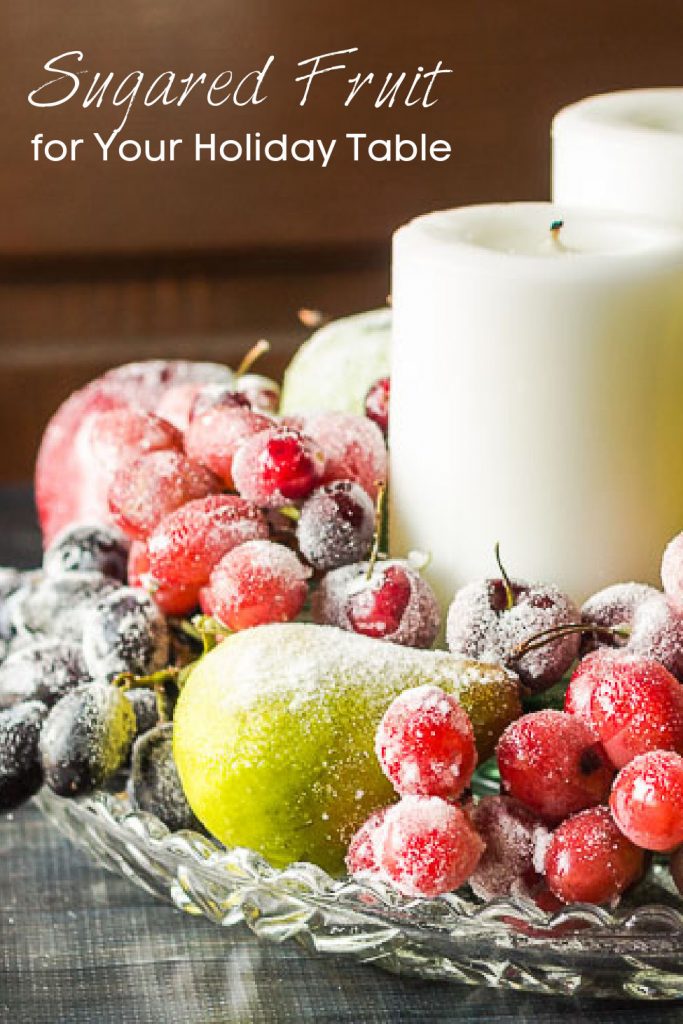 Side view of sugared fruit centerpiece on a glass tray with white candles.
