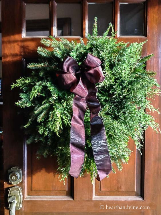 Fresh evergreen wreath on front door with wine colored bow.