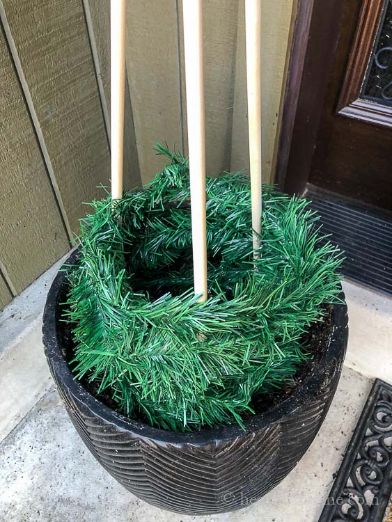Fake garland being wrapped around three wood dowel rods in a garden planter.