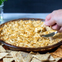 Hot Maryland Crab Dip with cracker and a hand dipping into it with a cracker.
