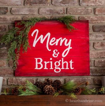 Merry and bright red sign with white letter on mantel with greenery on the top left corner