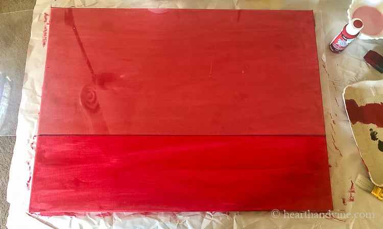 A red painted canvas in a landscape view with a piece of plexiglass lying on top cover 2/3 of the top and a dark line drawn at the bottom.