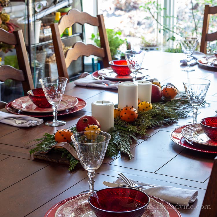 Dining room table set with red and white dishes and a DIY pallet centerpiece with cedar, white candles and fruit.