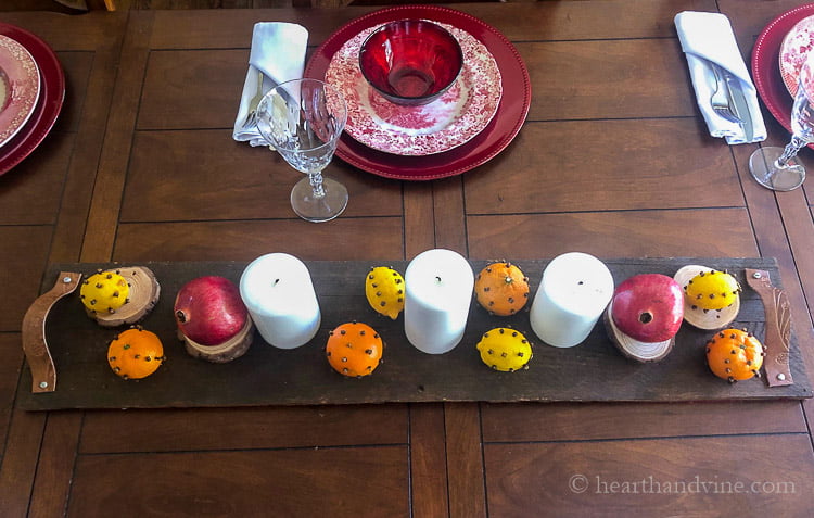 Wood pallet tray with white candles, pomegranates, and clove studded lemons and clementines.