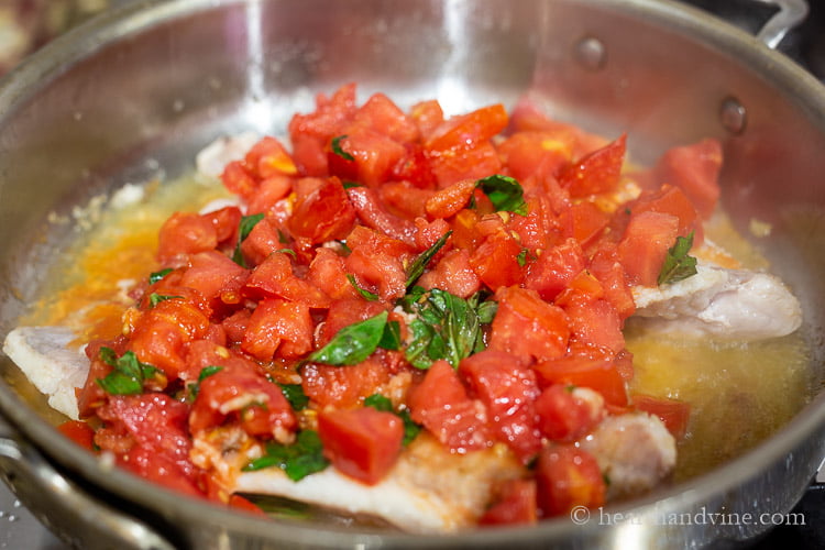 Tomatoes and basil on top of fish fillets in a frying pan.