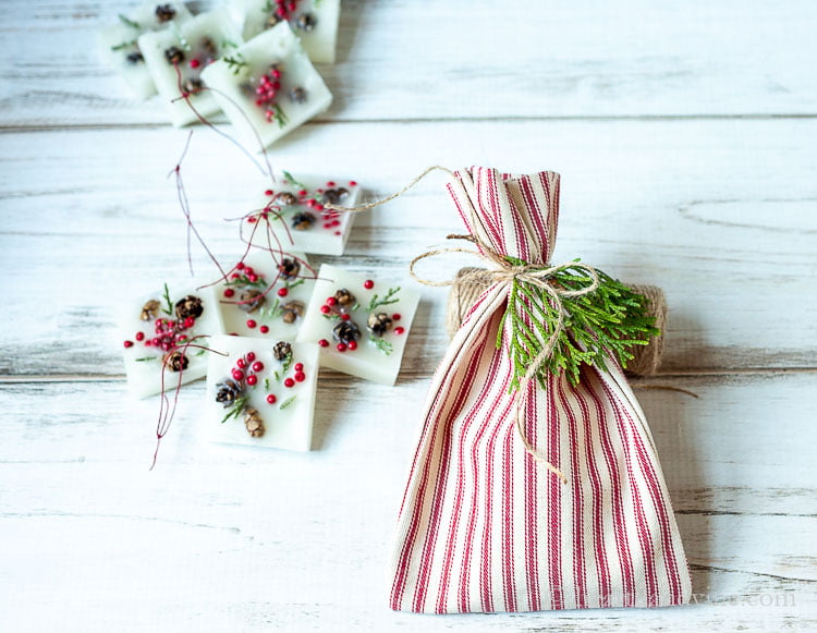 Christmas wax scented ornament in a small pile next to a red and white striped fabric bag with a twine ribbon and some fresh greenery.