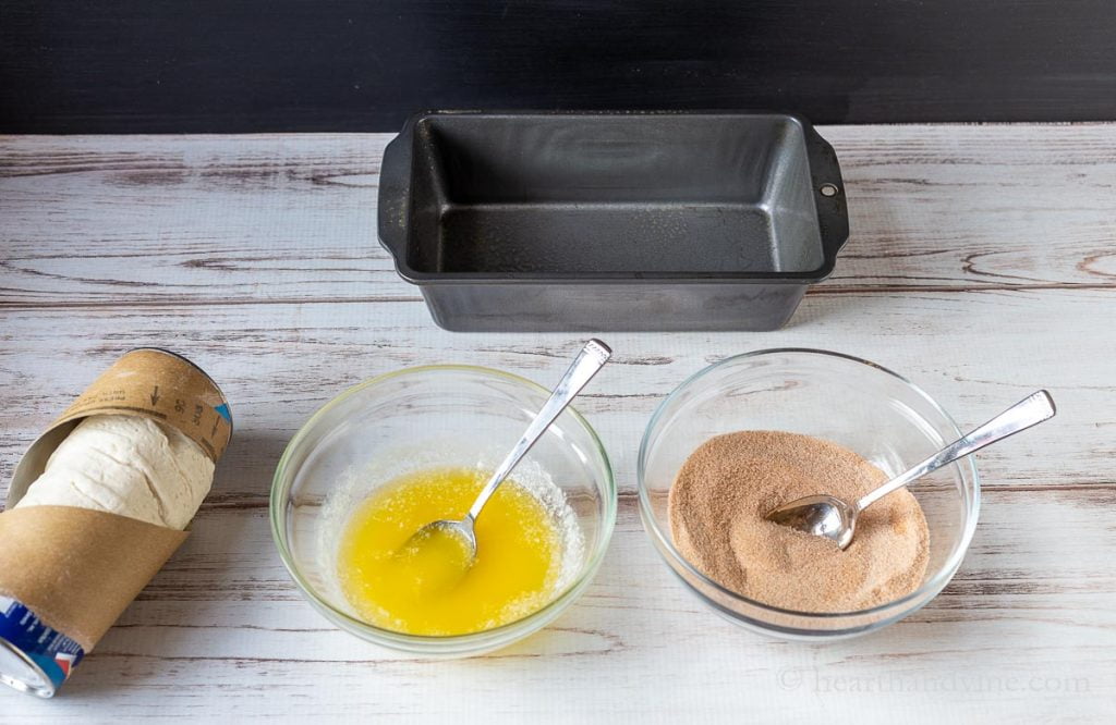 Bowls of melted butter and cinnamon sugar, a loaf pan and a package of refrigerator biscuits.