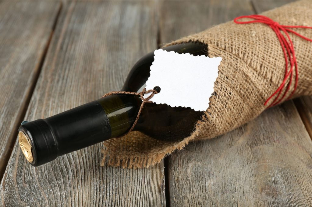 Wine bottle wrapped in burlap with a tag.