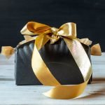 Black paper plate box with gold ribbon.
