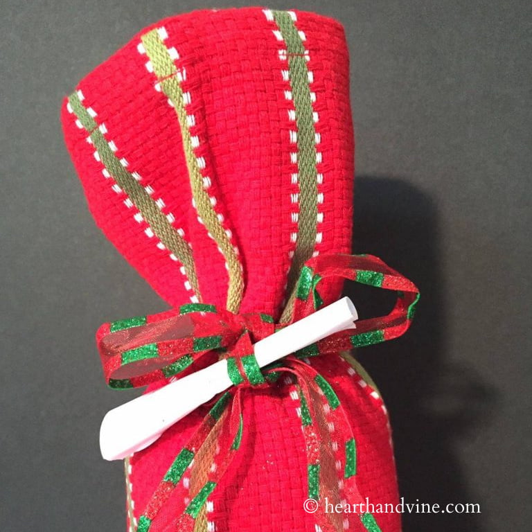 Wine bottle wrapped in red and green tea towel with a small paper scroll