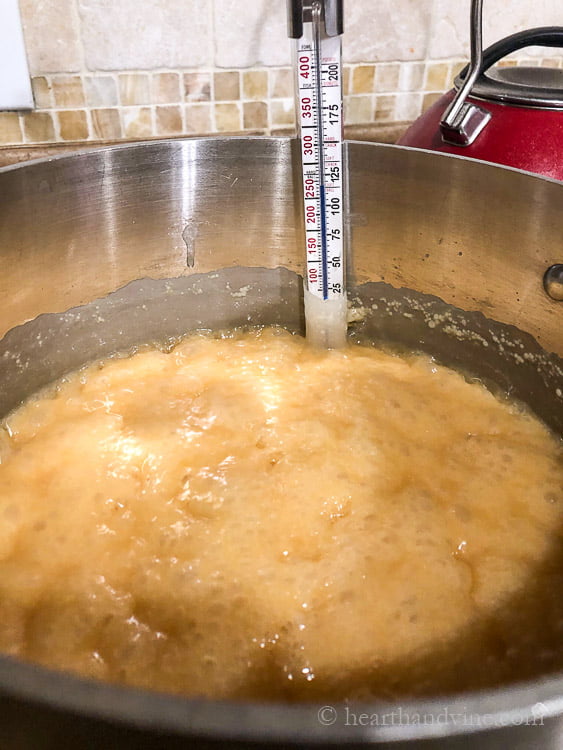 Caramel mixture bubbling in a large saucepan with a candy thermometer.