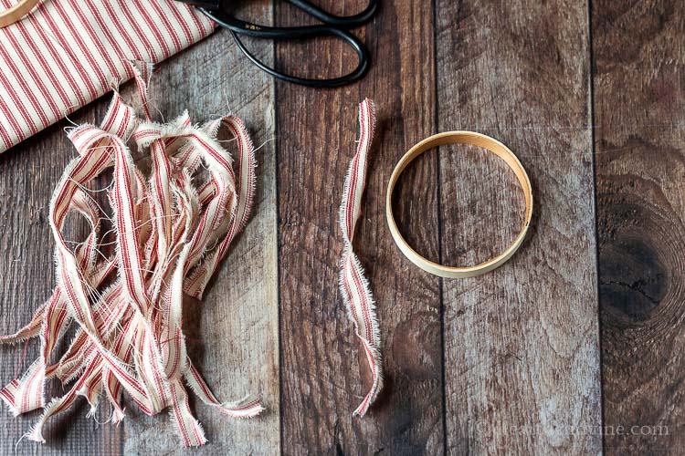 Small wooden embroidery hoop next to several strips of red and white fabric and a black pair of scissors.