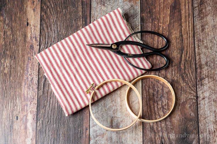 Red and white ticking fabric, mini wooden embroidery hoop and black scissors.