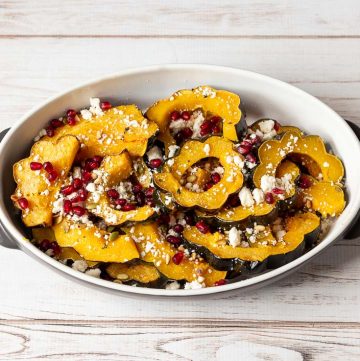 Pan of sliced roasted acorn squash with pine nut, pomegranate seeds and queso fresco.