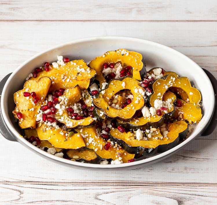 Pan of sliced roasted acorn squash with pine nut, pomegranate seeds and queso fresco.