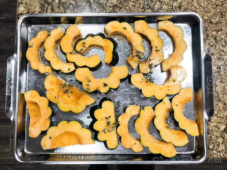 Sliced acorn squash on a cookie sheet with a few thyme stems, salt and pepper.