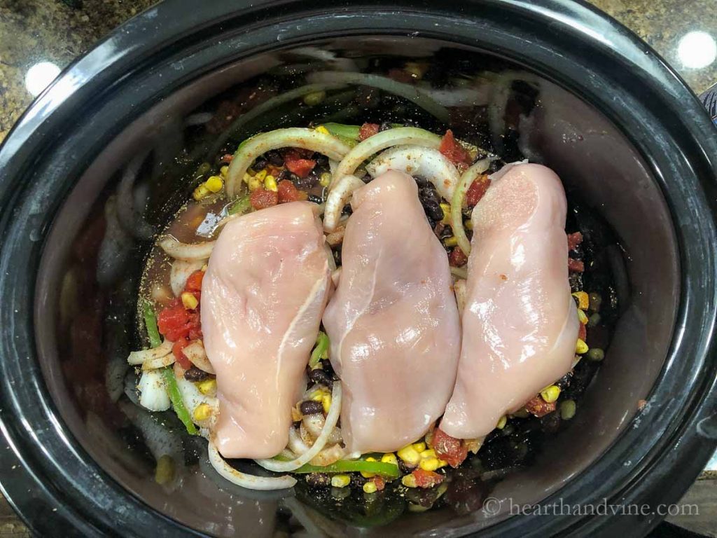Slow cooker with vegetables, beans, corn spices and 3 boneless chicken breasts.