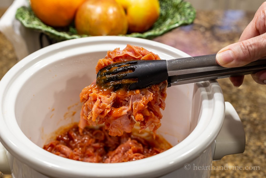 Ham barbecue in a slow cooker with tongs