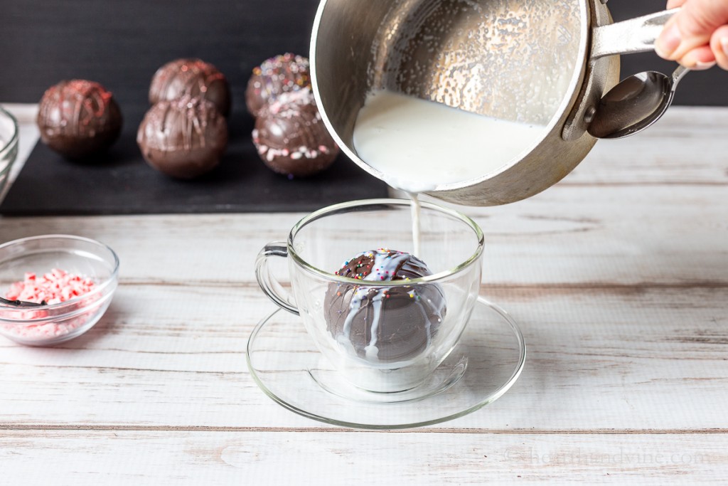 Pouring hot milk from a pan into a cup with a chocolate bomb.