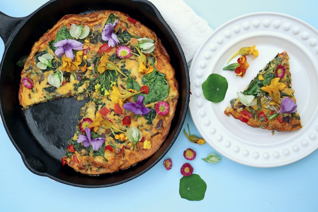 Cast iron skillet with a frittata and edible flowers next to a plate with a piece of the frittata.