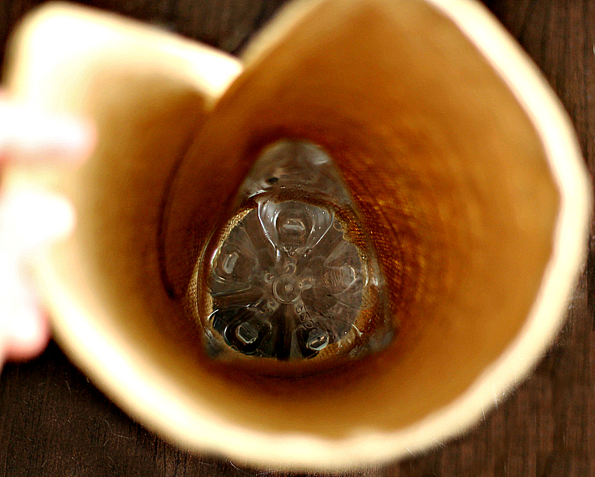 The bottom of a plastic water bottle fitted inside a burlap vase.