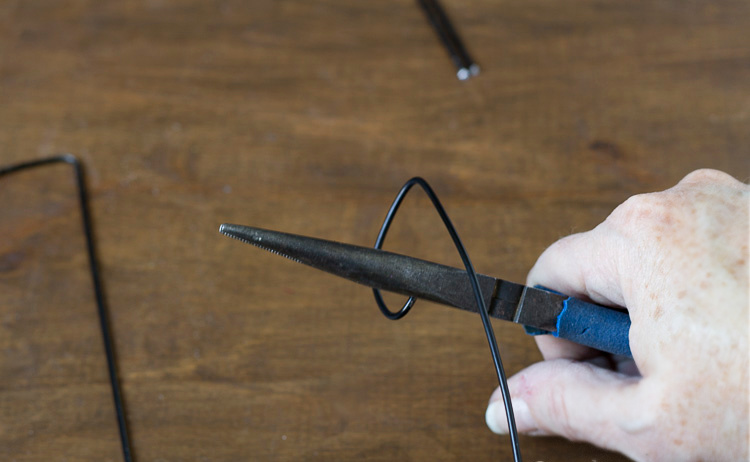 Using needle-nose pliers to shape the top of a hook on a piece of wire hanger.