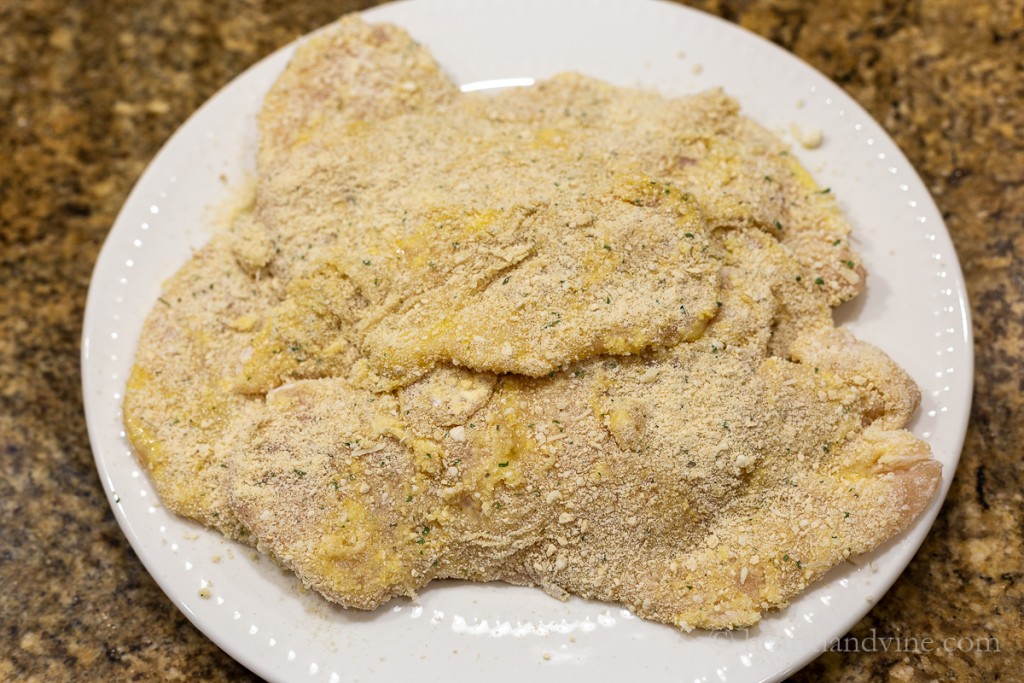 Thin boneless, skinless chicken breast cutlets breaded and stacked on a plate.