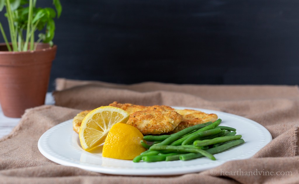 Chicken Romano on a plate with lemon wedges and green beans.