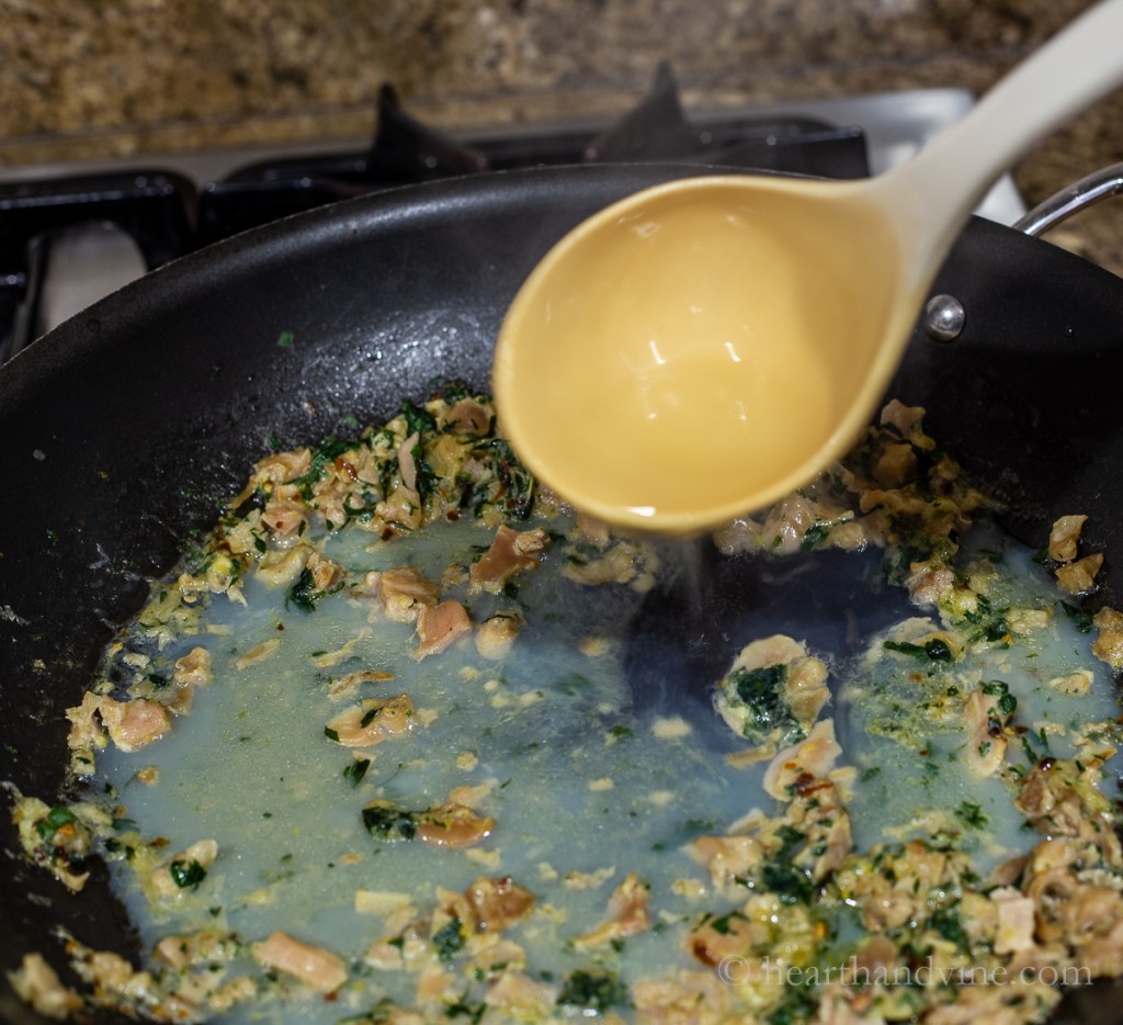 Adding pasta water to the pan with clam sauce.