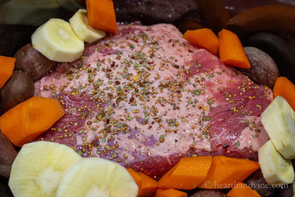 Brined corned beef with pickled seasoning in a slow cooker with cut up vegetables.