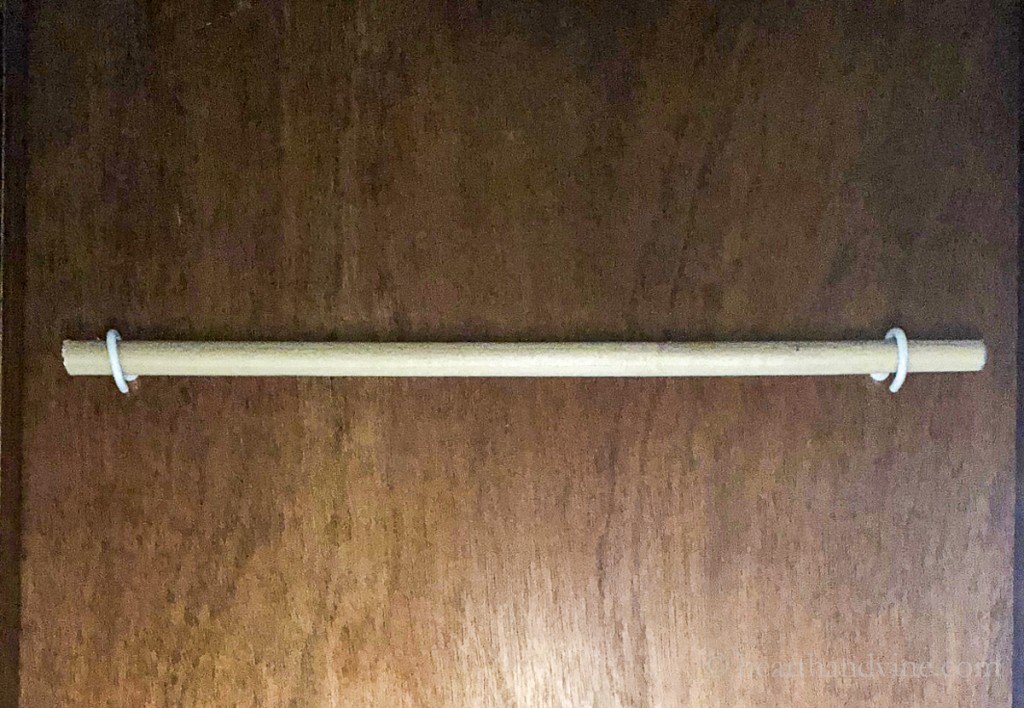 Wooden dowel rod hung under a cabinet with two cup hooks.