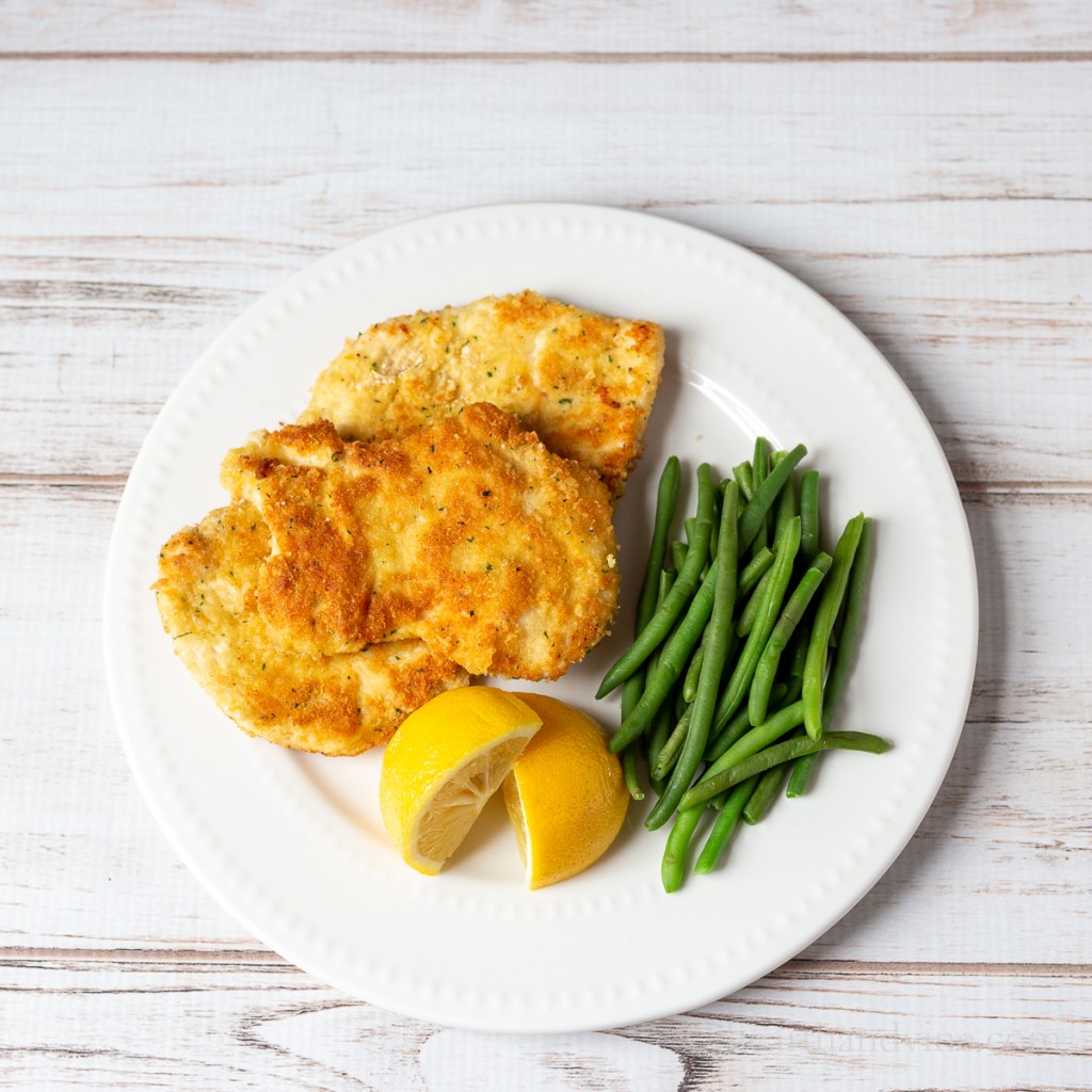 Chicken Romano on a plate with lemon wedges and green beans.