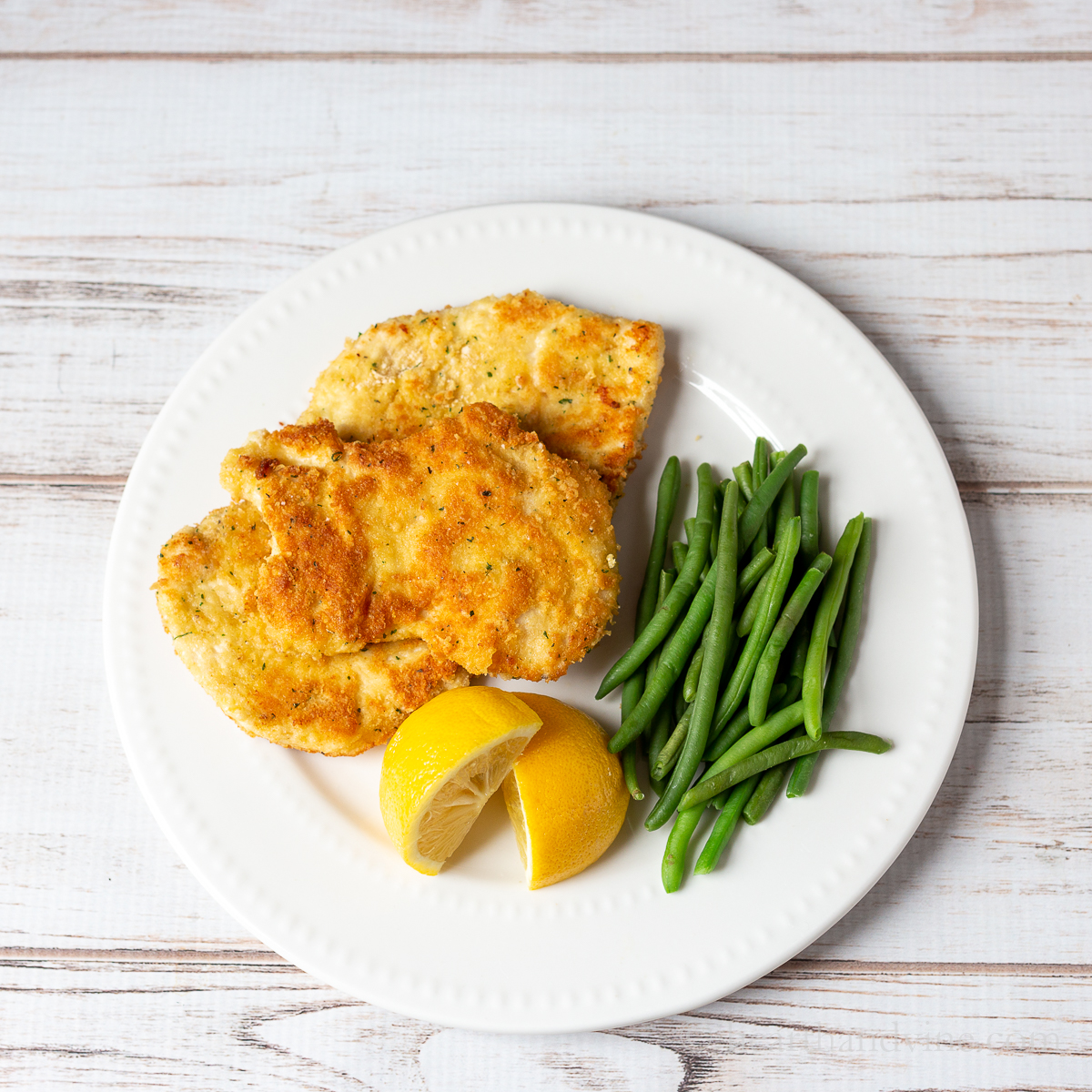 Plate of chicken Romano with lemon wedges and green beans