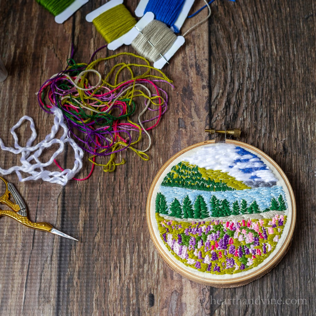 Small landscape embroidery art hoop, threads and scissors.