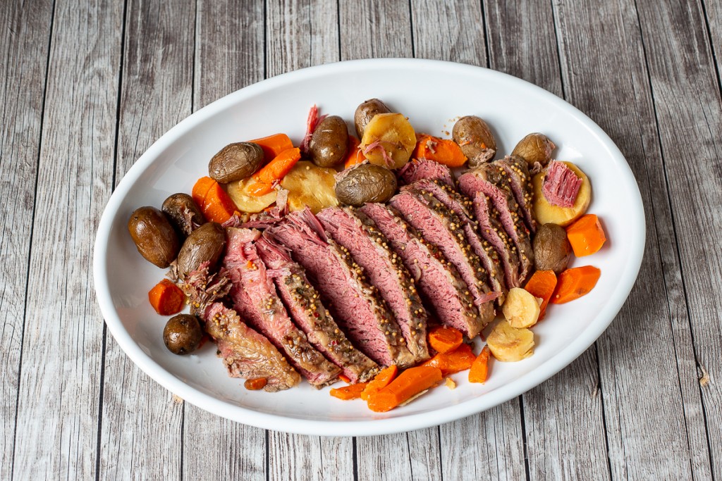 Sliced roast corned beef on a large platter with red potatoes, carrots and parsnips.