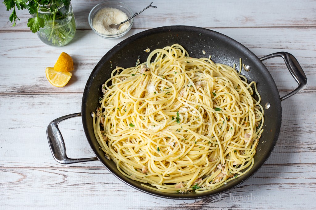 Large skillet with spaghetti and clam sauce dressed with grated Parmesan cheese.