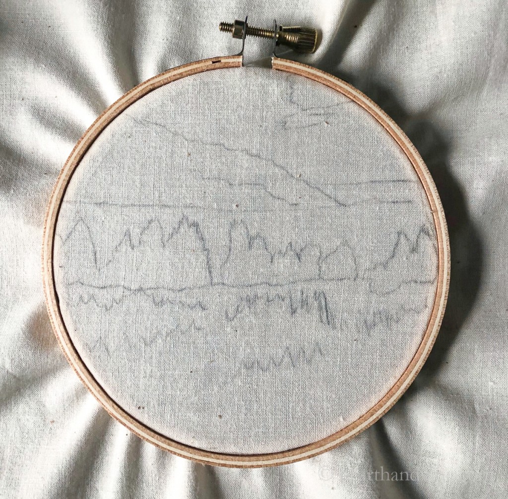 Traced landscape image on muslin in an embroidery hoop.